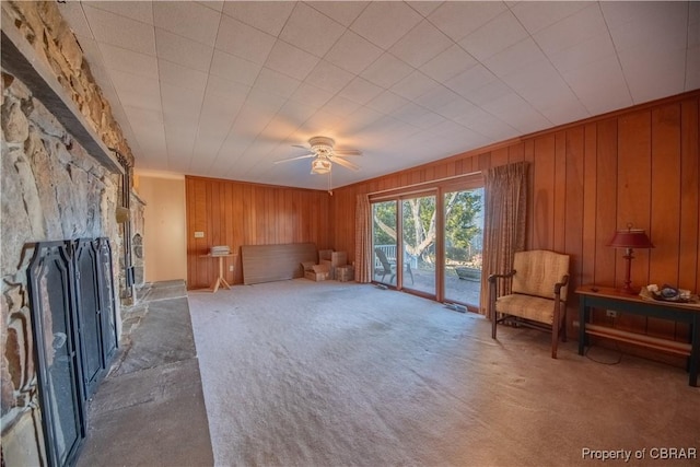 carpeted living area with a ceiling fan, a fireplace, and wood walls