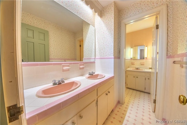 bathroom with a wainscoted wall, a sink, and wallpapered walls