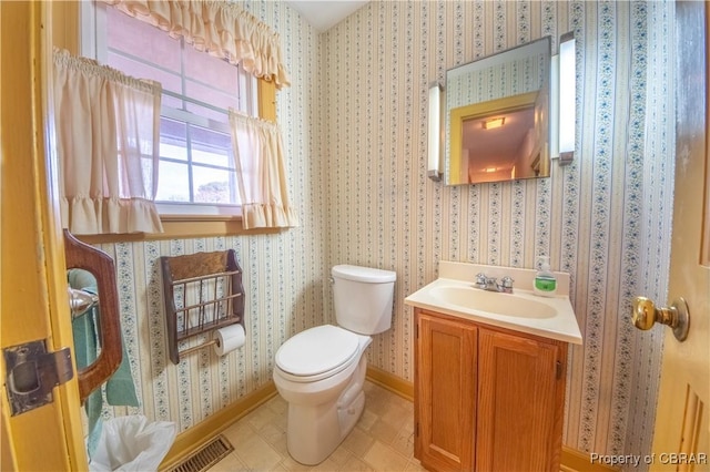 bathroom featuring toilet, visible vents, baseboards, vanity, and wallpapered walls