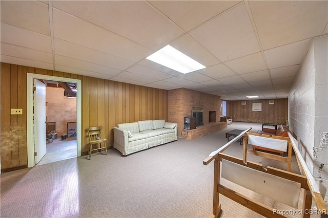 living area with a brick fireplace, a drop ceiling, and wood walls