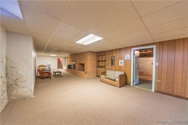 unfurnished room with a brick fireplace, light carpet, wood walls, and a drop ceiling