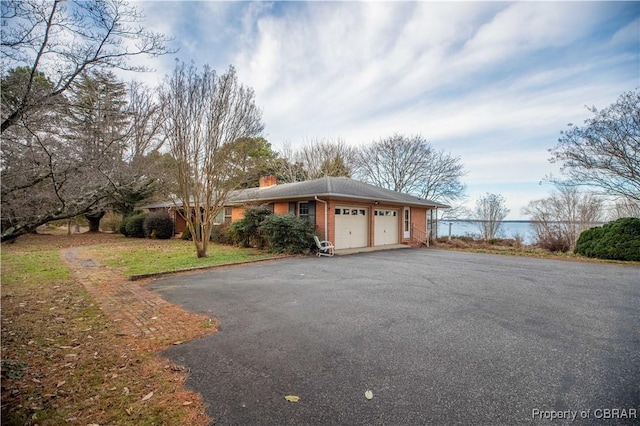 ranch-style home with a garage, driveway, brick siding, and a chimney