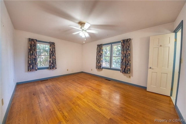 unfurnished bedroom featuring a ceiling fan, multiple windows, light wood-style flooring, and baseboards