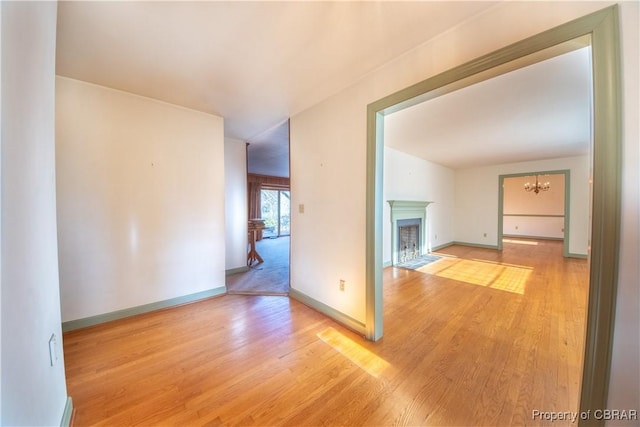 unfurnished room featuring light wood finished floors, a fireplace with flush hearth, baseboards, and a notable chandelier