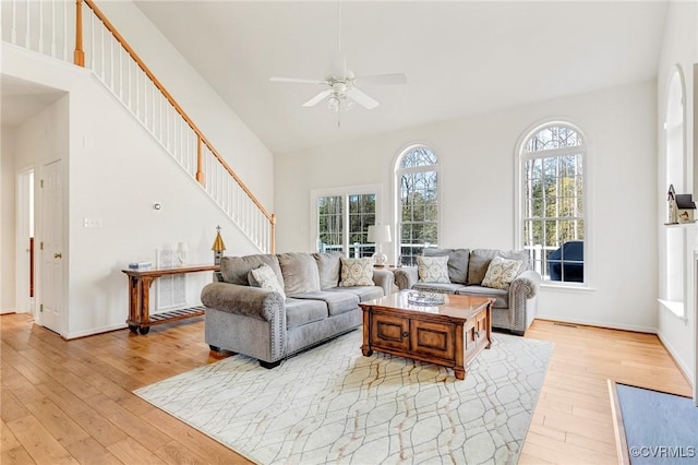 living room featuring ceiling fan, a towering ceiling, and light hardwood / wood-style floors