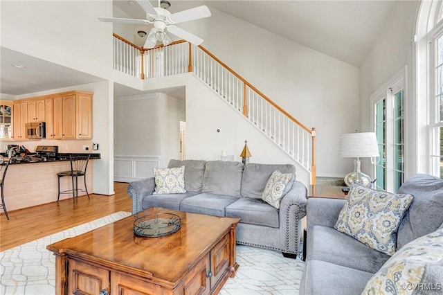 living room featuring ceiling fan, a healthy amount of sunlight, a high ceiling, and light wood-type flooring