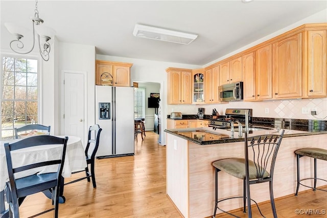 kitchen featuring appliances with stainless steel finishes, a breakfast bar, backsplash, kitchen peninsula, and light wood-type flooring