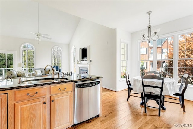 kitchen with sink, dark stone counters, hanging light fixtures, stainless steel dishwasher, and light hardwood / wood-style floors