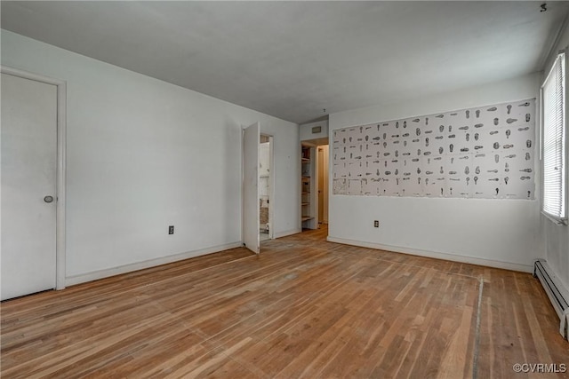 unfurnished room with a baseboard heating unit and light wood-type flooring