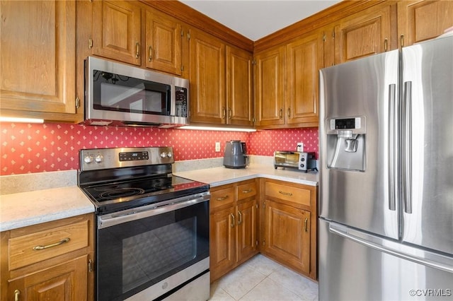 kitchen featuring stainless steel appliances, brown cabinetry, light countertops, and light tile patterned flooring