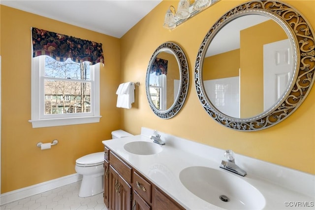 full bathroom featuring toilet, double vanity, baseboards, and a sink