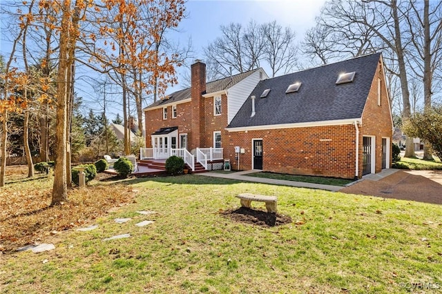 back of property with brick siding, a yard, driveway, a wooden deck, and a chimney