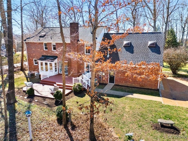 back of property featuring a yard, brick siding, a chimney, and a wooden deck