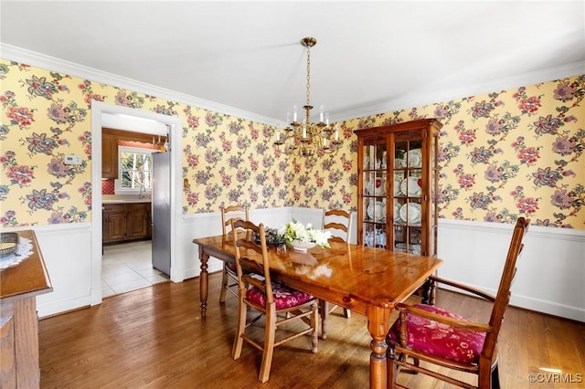 dining area with a wainscoted wall, a chandelier, wood finished floors, and wallpapered walls