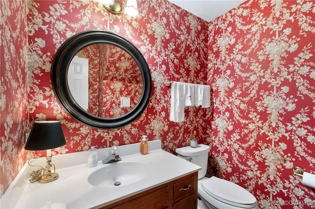 half bathroom featuring toilet, wallpapered walls, and vanity