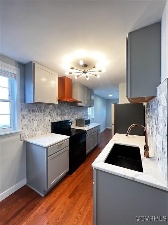 kitchen featuring black / electric stove, tasteful backsplash, sink, gray cabinetry, and wall chimney exhaust hood