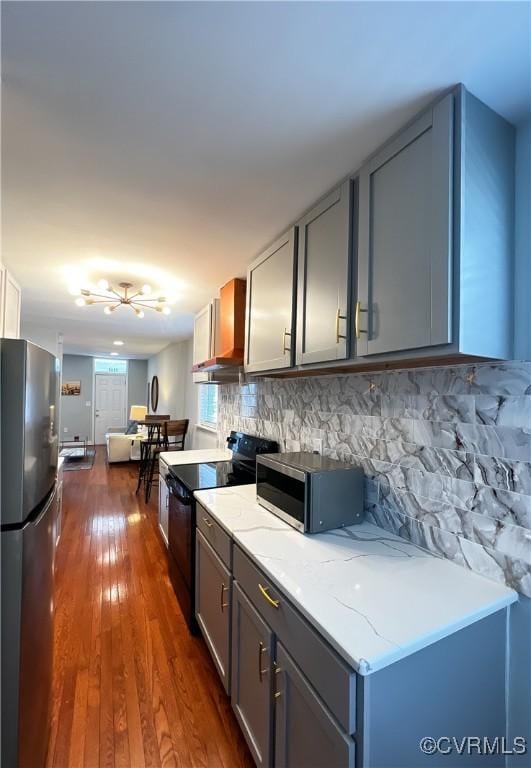 kitchen featuring gray cabinetry, appliances with stainless steel finishes, dark hardwood / wood-style flooring, light stone countertops, and wall chimney range hood