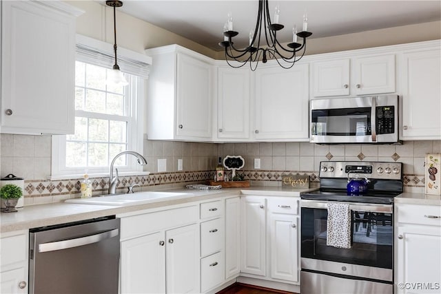 kitchen featuring appliances with stainless steel finishes, decorative light fixtures, light countertops, white cabinetry, and a sink