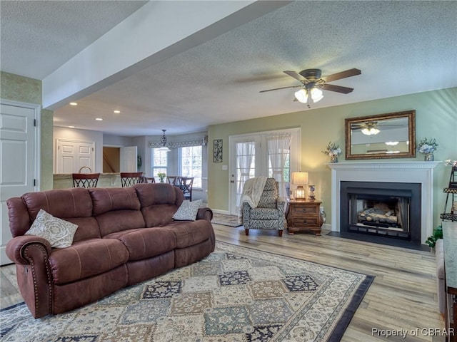 living room with recessed lighting, a fireplace with flush hearth, light wood-style floors, a textured ceiling, and baseboards