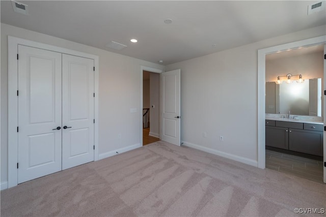 unfurnished bedroom featuring sink, light carpet, ensuite bath, and a closet