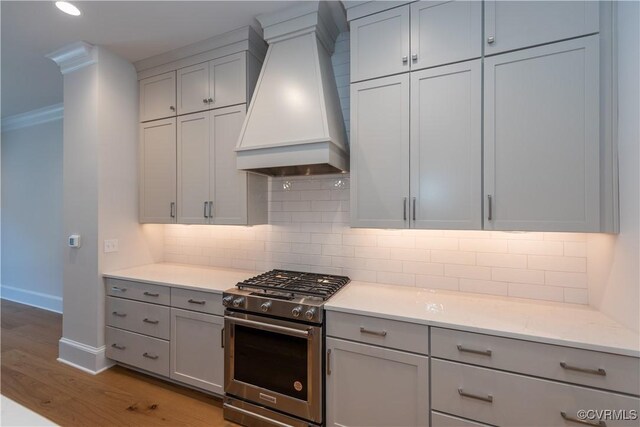 kitchen featuring light hardwood / wood-style flooring, stainless steel range with gas cooktop, custom range hood, and tasteful backsplash