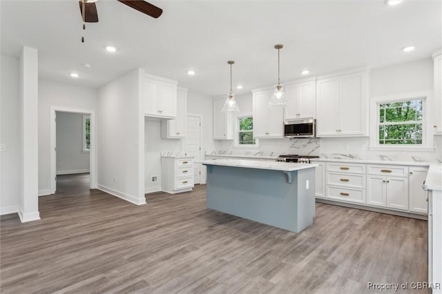 8280 Mobjack Ln, Hayes, VA 23072 - kitchen with stainless steel microwave, a healthy amount of sunlight, white cabinetry, and a center island