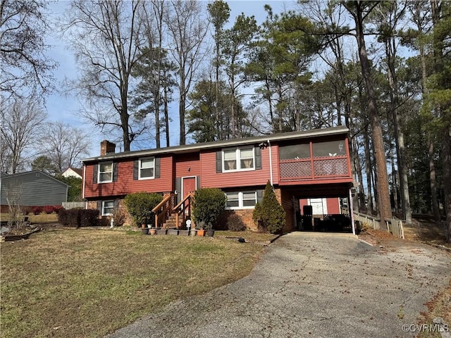 bi-level home featuring aphalt driveway, brick siding, a sunroom, a front lawn, and a chimney