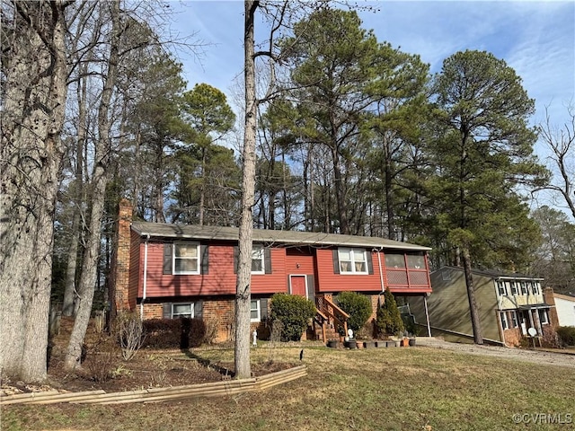 split foyer home with a sunroom, brick siding, a chimney, and a front lawn