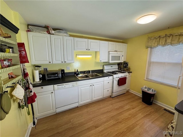 kitchen featuring dark countertops, white appliances, white cabinets, and a sink