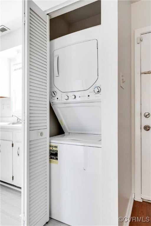 washroom featuring sink, light hardwood / wood-style flooring, and stacked washer / dryer