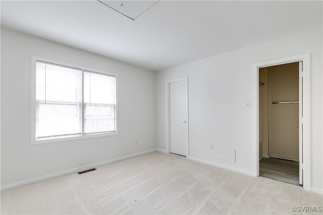 unfurnished bedroom with a walk in closet and light colored carpet