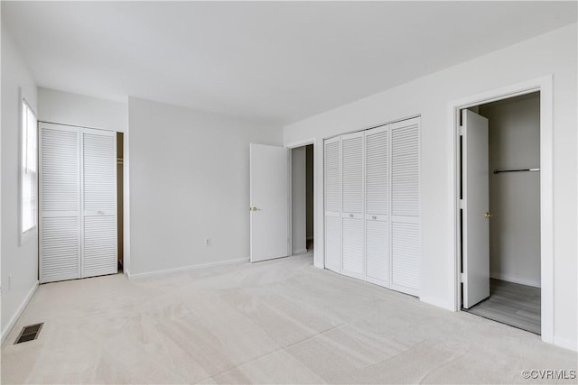 unfurnished bedroom featuring light carpet, two closets, and multiple windows