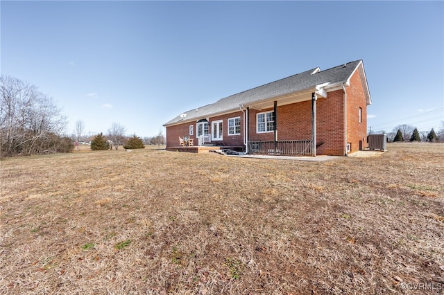 rear view of house with cooling unit, a lawn, and brick siding