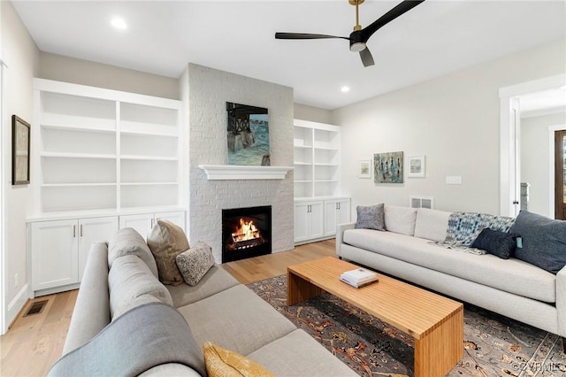 living room featuring ceiling fan, built in features, a fireplace, and light hardwood / wood-style flooring