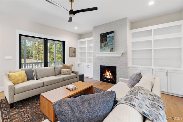 living room featuring a brick fireplace, hardwood / wood-style flooring, built in features, and ceiling fan