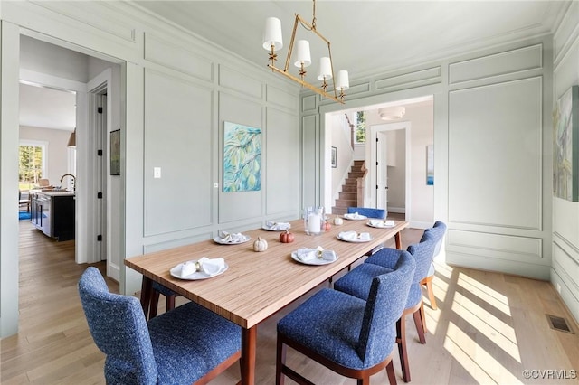 dining room with an inviting chandelier, sink, light hardwood / wood-style flooring, and ornamental molding