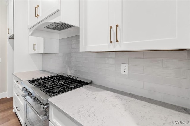 kitchen featuring white cabinetry, high end stainless steel range oven, light stone countertops, light hardwood / wood-style floors, and backsplash