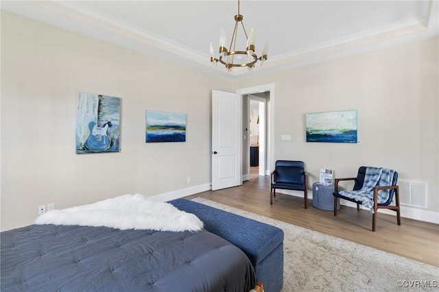 bedroom with wood-type flooring, ornamental molding, a notable chandelier, and a tray ceiling