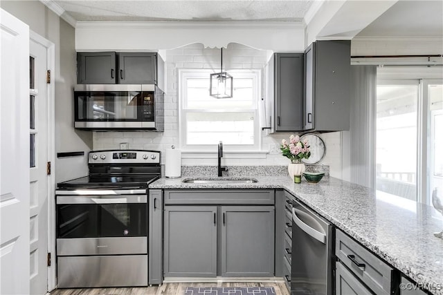 kitchen featuring stainless steel appliances, gray cabinetry, ornamental molding, a sink, and plenty of natural light