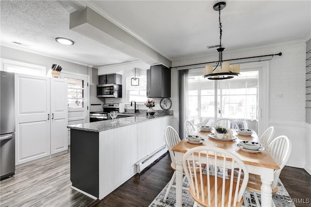 kitchen featuring crown molding, a baseboard radiator, appliances with stainless steel finishes, wood finished floors, and a peninsula