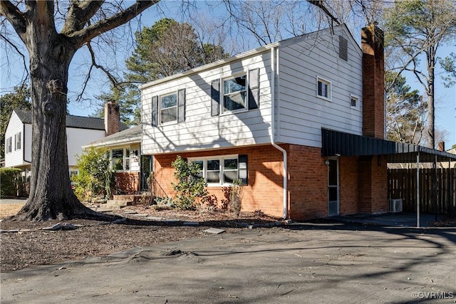 view of front of home featuring brick siding, fence, and a chimney