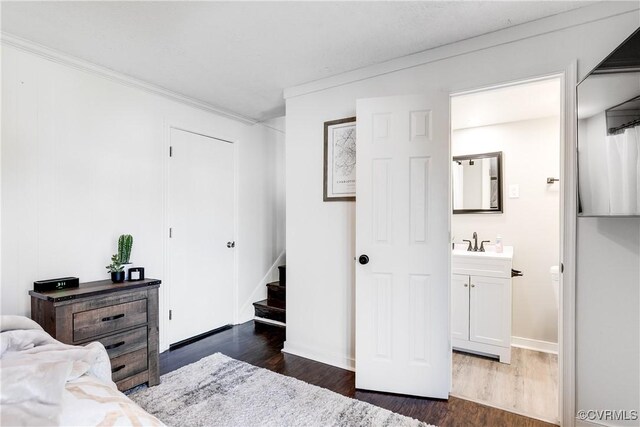 bedroom with dark wood-style floors, baseboards, crown molding, and a sink