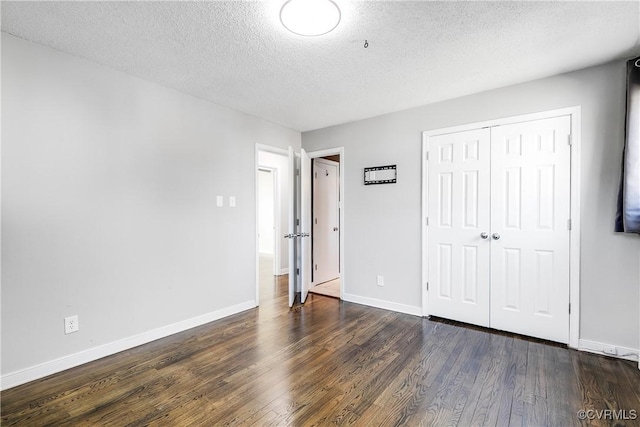 unfurnished bedroom featuring a textured ceiling, a closet, wood finished floors, and baseboards