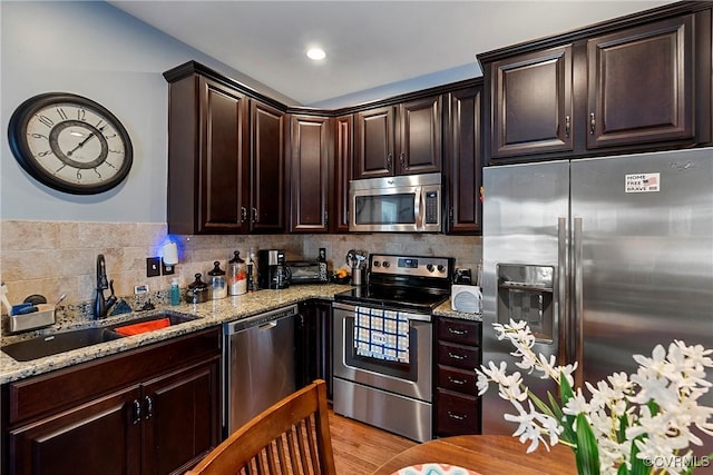 kitchen featuring sink, decorative backsplash, light stone counters, dark brown cabinetry, and stainless steel appliances