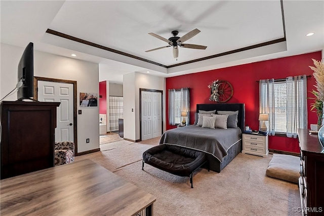 carpeted bedroom featuring a closet, ensuite bath, a raised ceiling, and ceiling fan