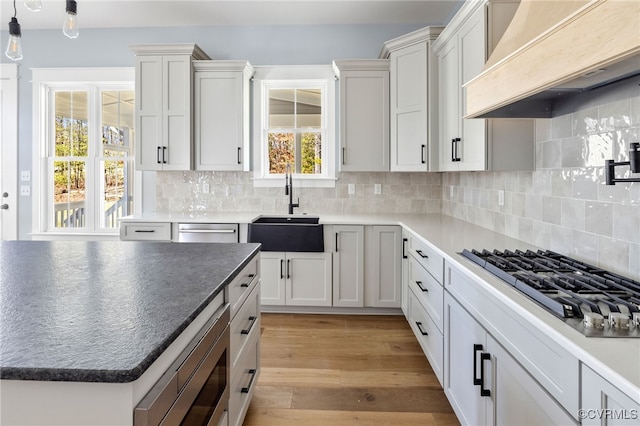 kitchen with sink, backsplash, stainless steel appliances, custom exhaust hood, and light wood-type flooring