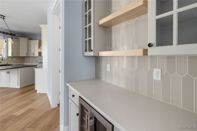 kitchen featuring sink, wine cooler, decorative backsplash, hanging light fixtures, and light hardwood / wood-style floors