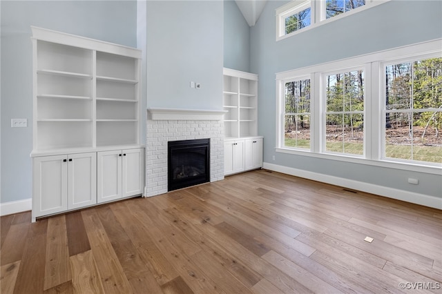 unfurnished living room featuring a brick fireplace, light hardwood / wood-style flooring, and a high ceiling