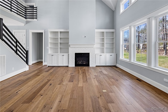 unfurnished living room featuring a towering ceiling, a fireplace, and light wood-type flooring