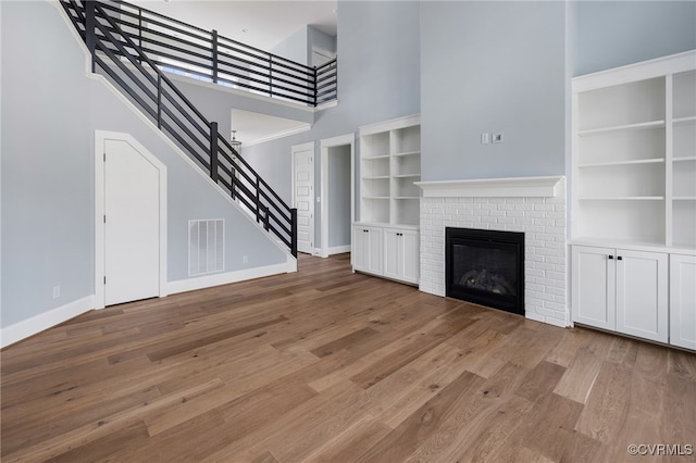 unfurnished living room with a towering ceiling, a fireplace, and light wood-type flooring